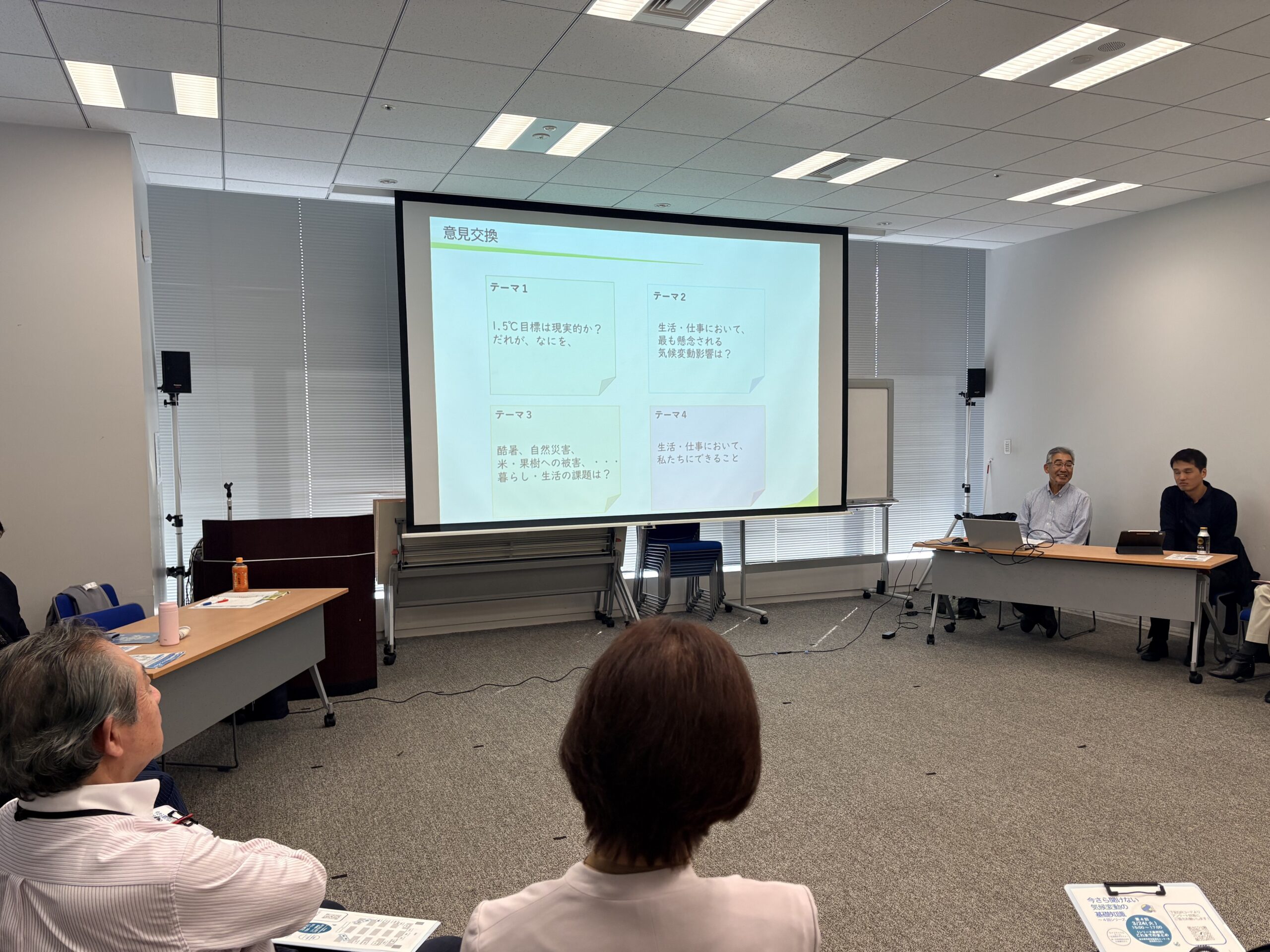 エコまちサークル第４回の様子。中央にスクリーンがある。参加者は車座で円形に座っている。