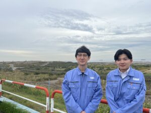 丹治さんと渡さんが処分場の前で並んで立っている様子の写真